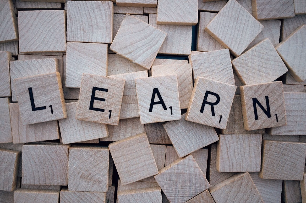 Wooden letter tiles arranged to spell learn on a background of scattered tiles.